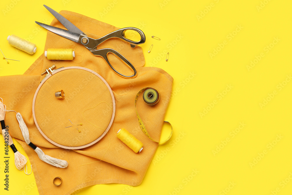 Embroidery hoop with canvas, mouline threads and measuring tape on yellow background