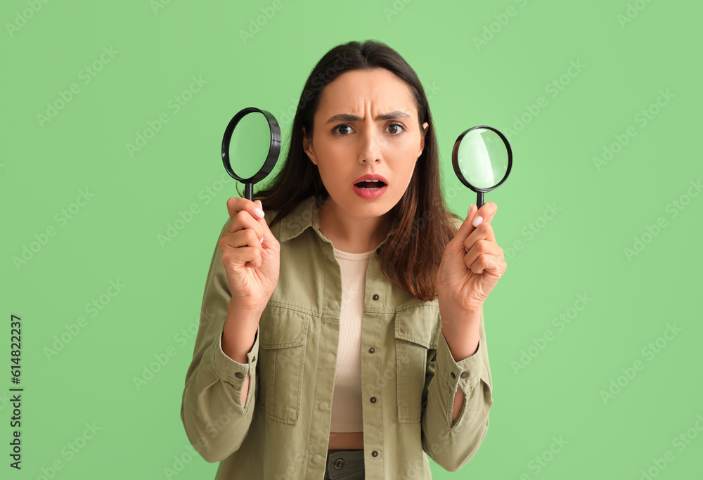 Upset young woman with magnifiers on green background