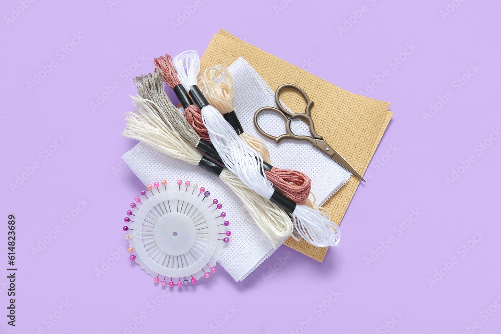 Different canvases with scissors, mouline threads and ball pins on lilac background