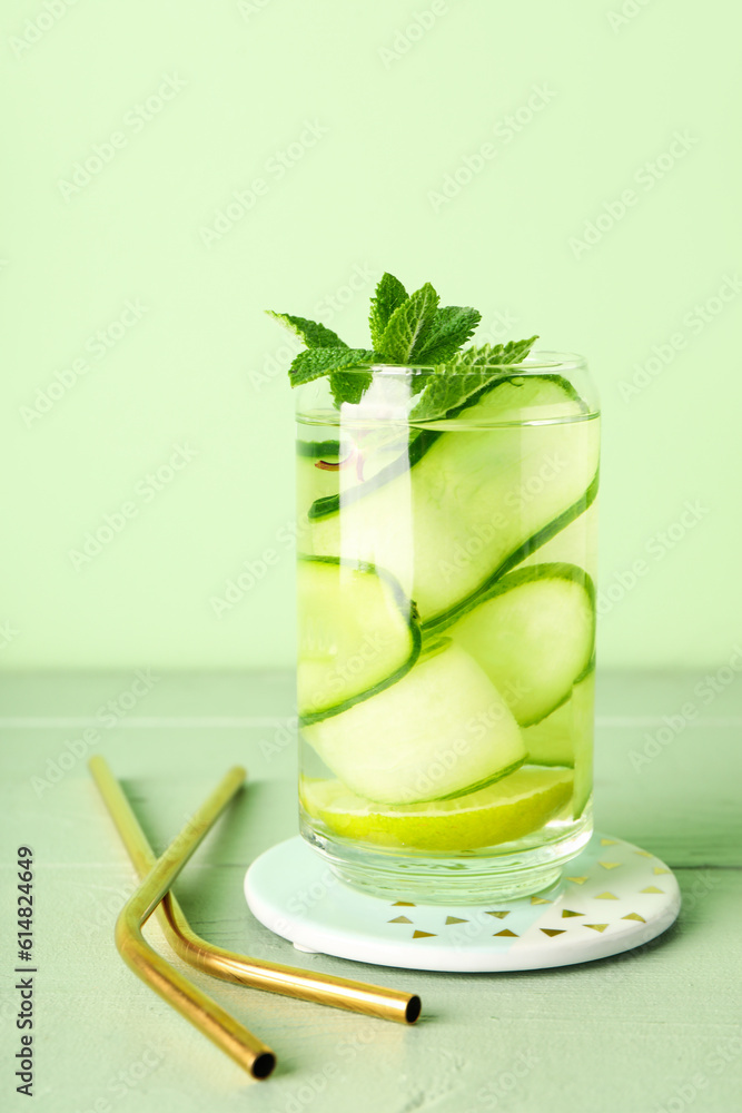 Glass of infused water with cucumber slices on green wooden table