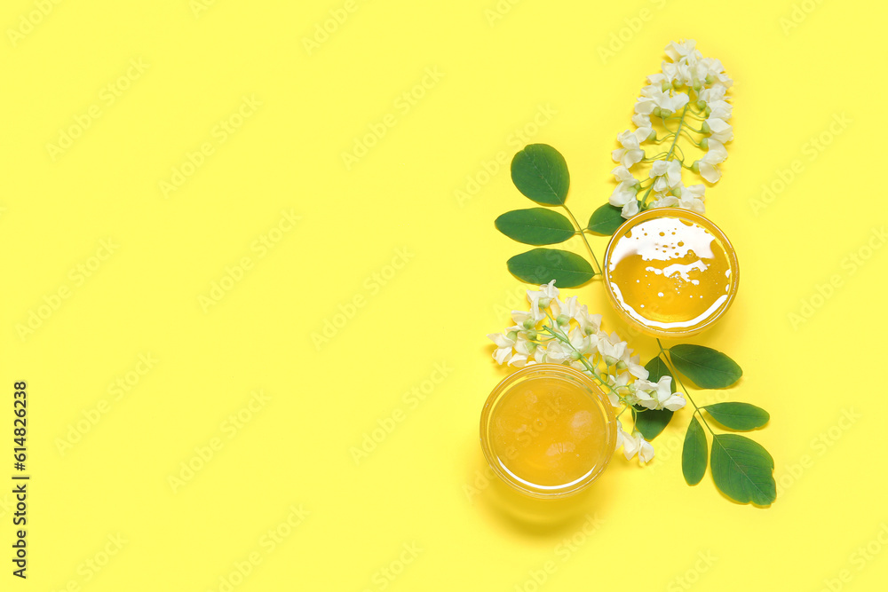 Bowls of honey with flowers of acacia on yellow background