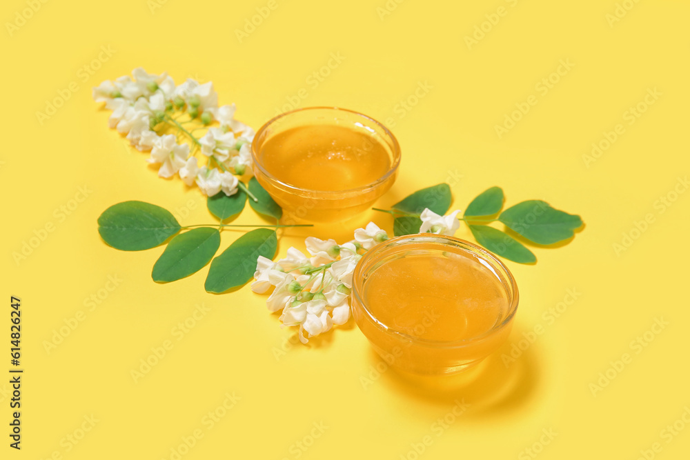 Bowls of honey with flowers of acacia on yellow background, closeup