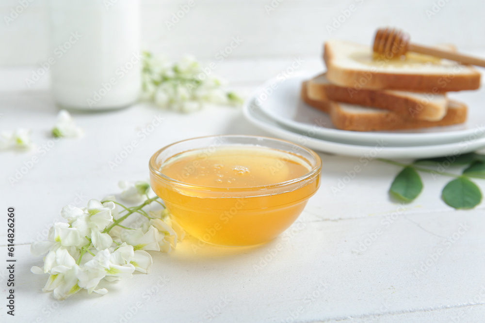 Bowl of honey with flowers of acacia and toasts on light wooden table, closeup