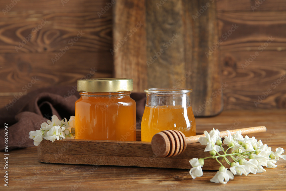 Jars of honey with flowers of acacia on wooden background, closeup