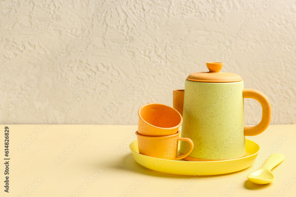 Plate with cups, teapot and spoon for baby on yellow table