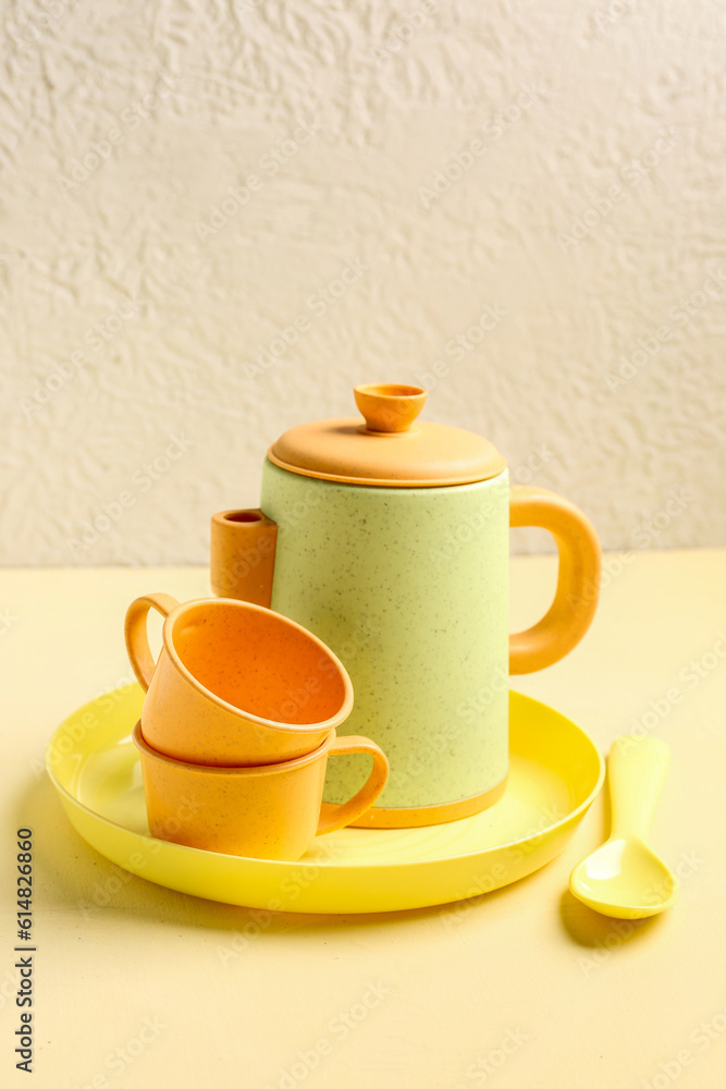 Plate with cups, teapot and spoon for baby on yellow table