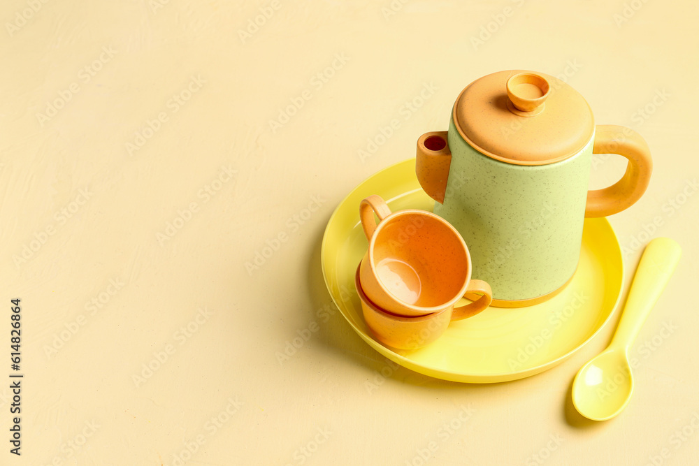 Plate with cups, teapot and spoon for baby on yellow table