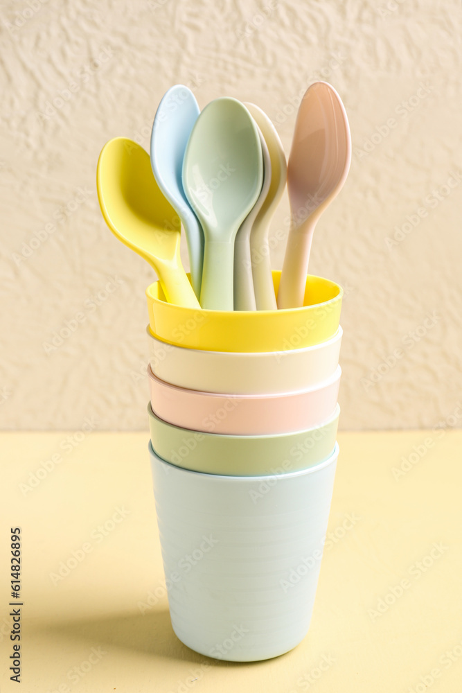 Colorful spoons and cups for baby on yellow table