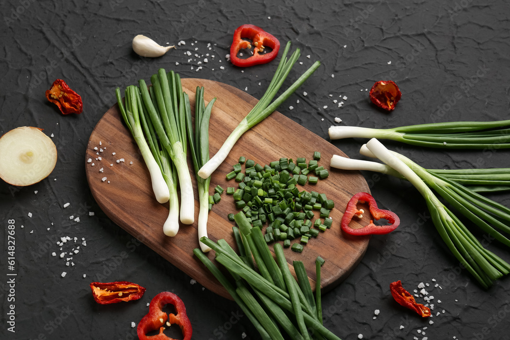 Board with slices of fresh green onion and pepper on black background