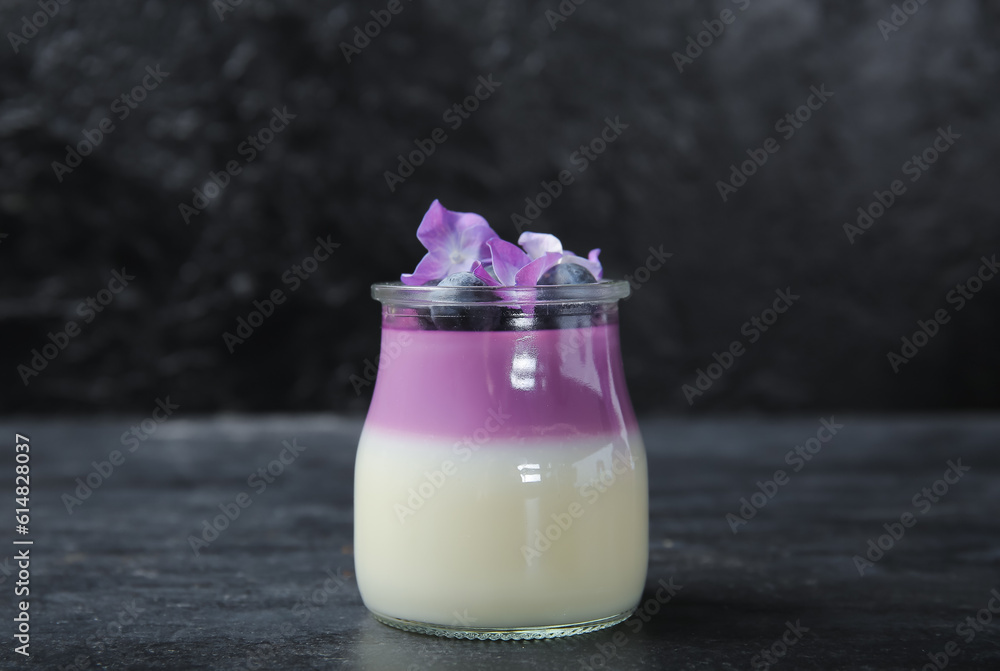 Glass of panna cotta with blueberry and beautiful hydrangea flowers on black table