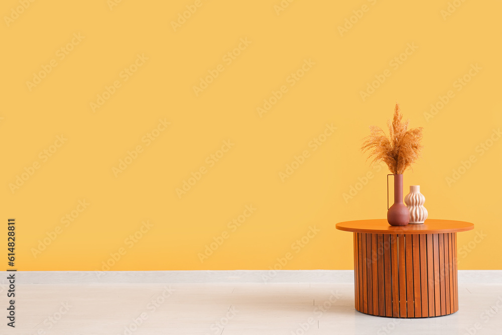 Wooden coffee table with pampas grass in vase near orange wall