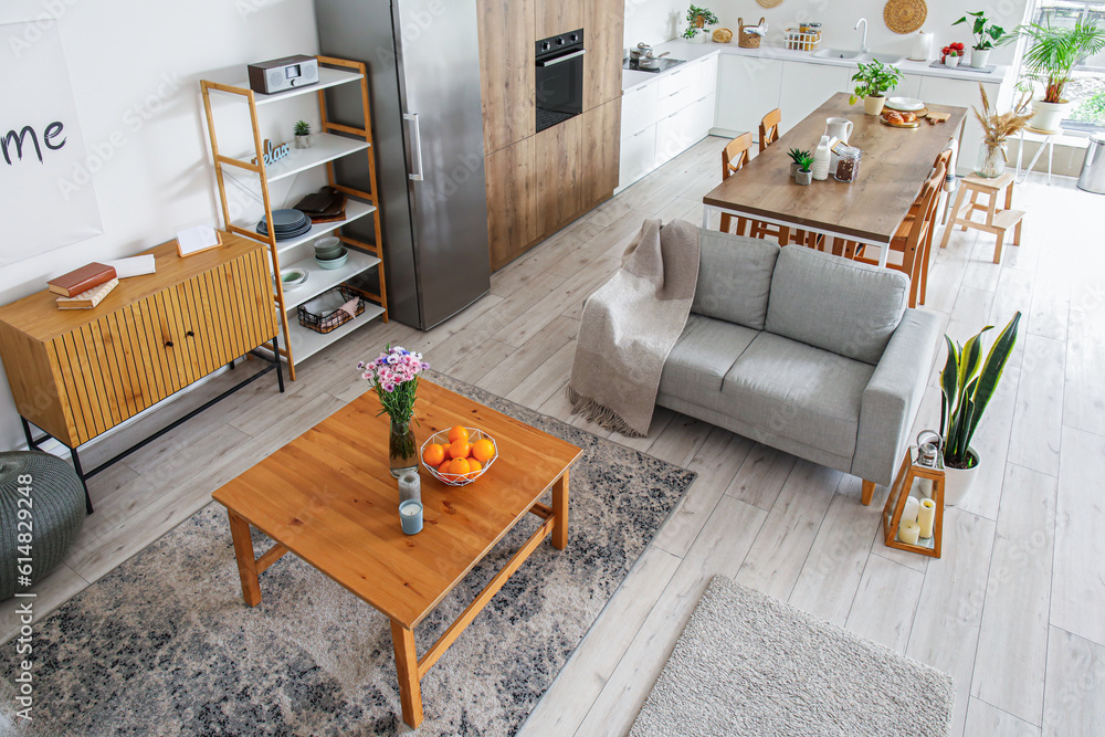 Interior of light open plan kitchen with fridge and grey sofa