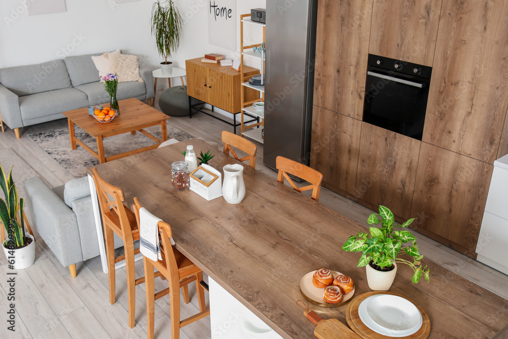 Interior of light open plan kitchen with island table and grey sofas