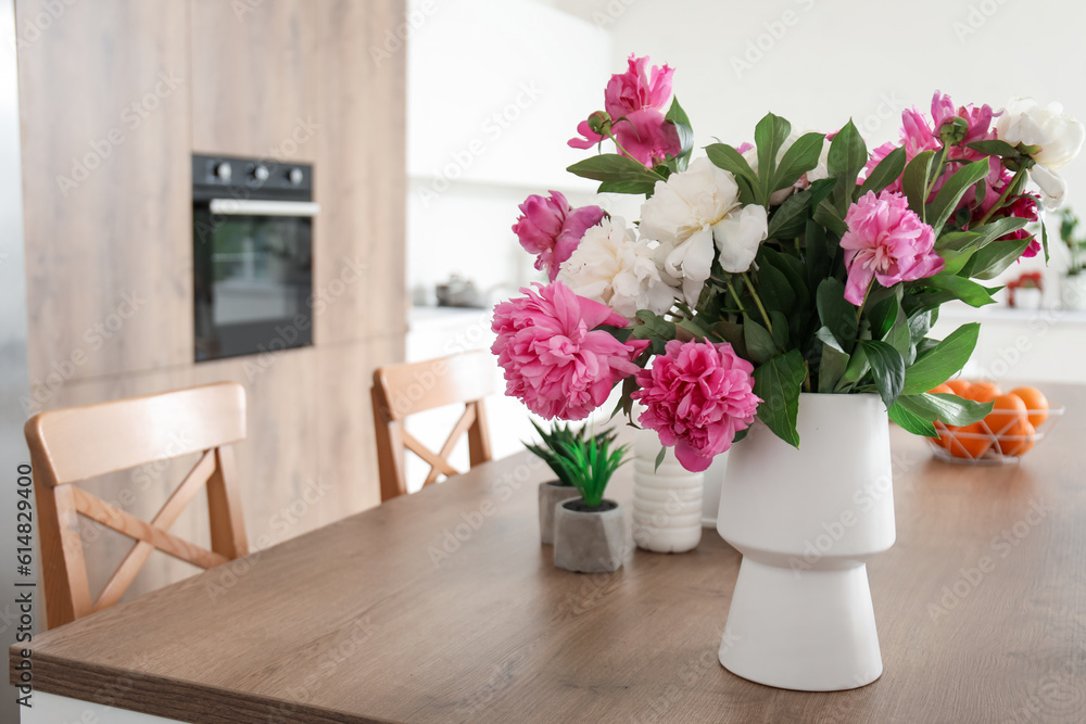 Vase with beautiful peony flowers on table in modern kitchen