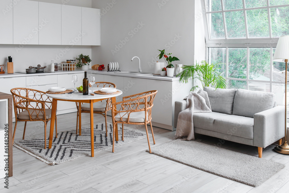 Interior of light open plan kitchen with served dining table and grey sofa