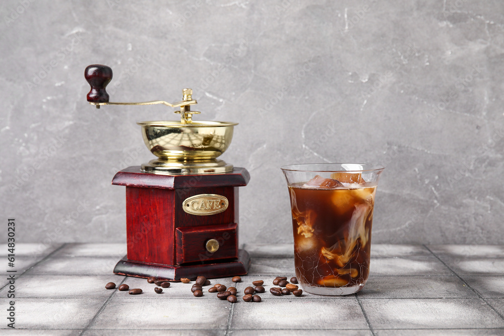 Glass of tasty ice coffee with milk and grinder on table