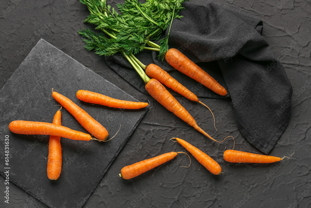 Board with fresh carrots on black background