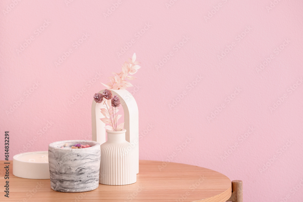 Holders with candles and decor on table near pink wall in room