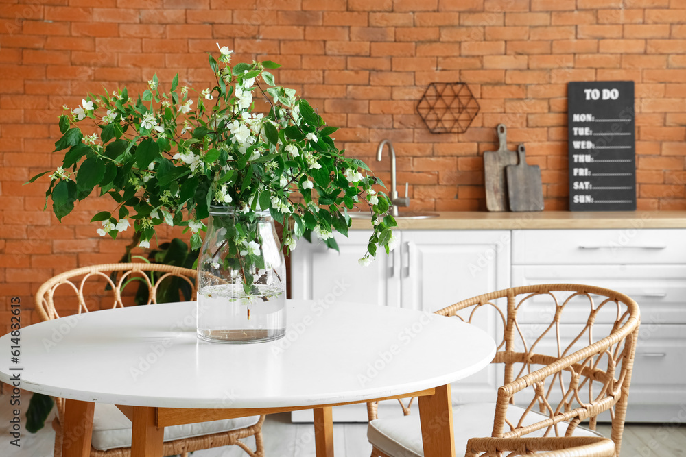 Vase with blooming jasmine flowers on dining table in kitchen