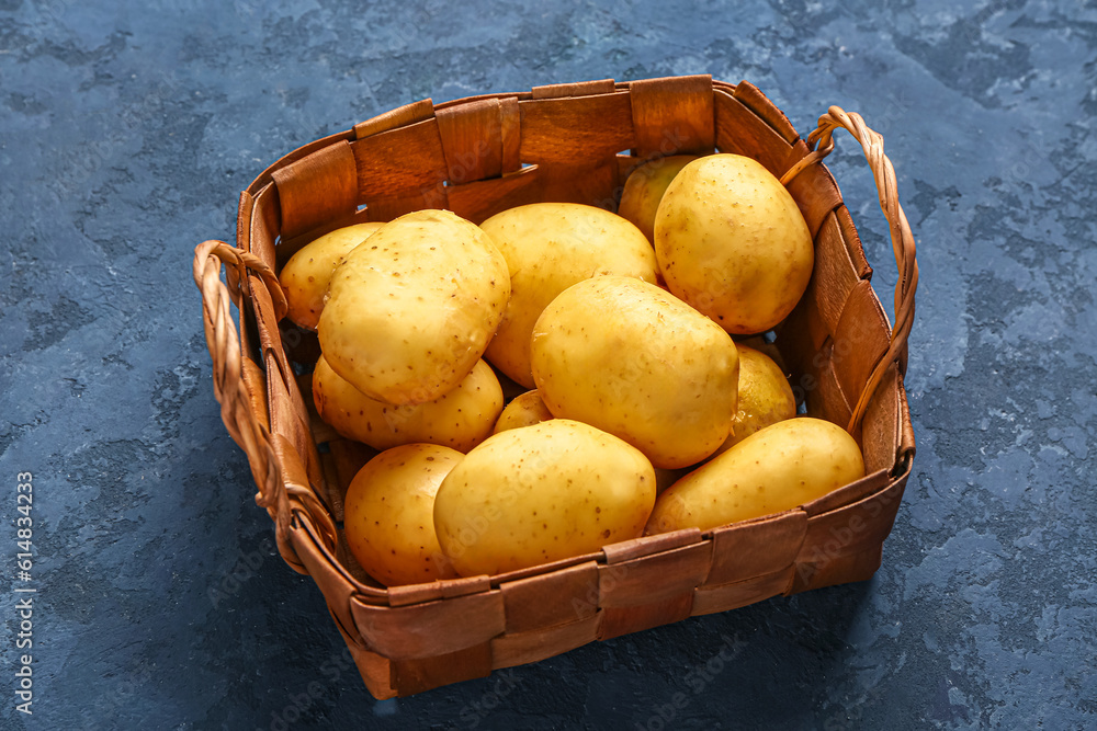 Wicker basket with raw baby potatoes on blue background