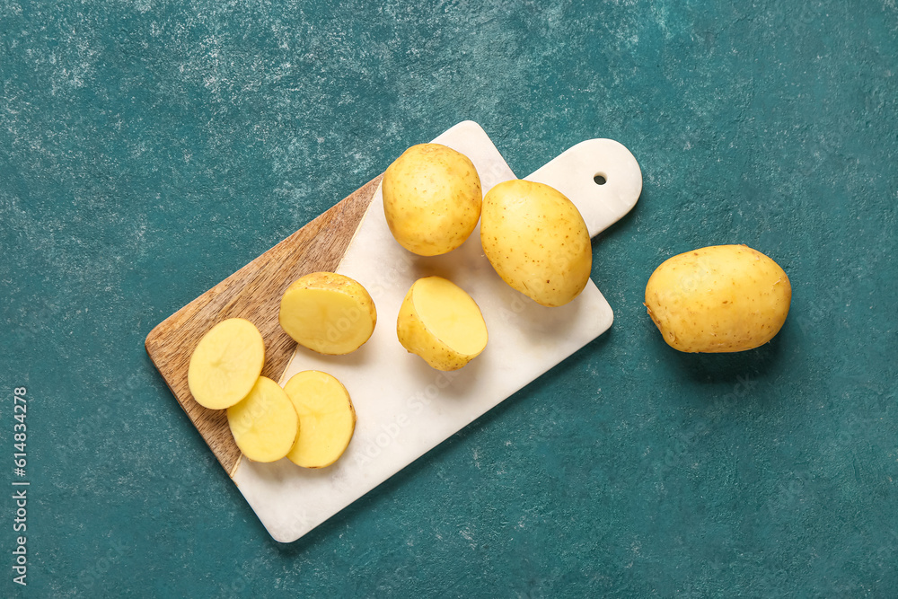 Board with raw baby potatoes on green background