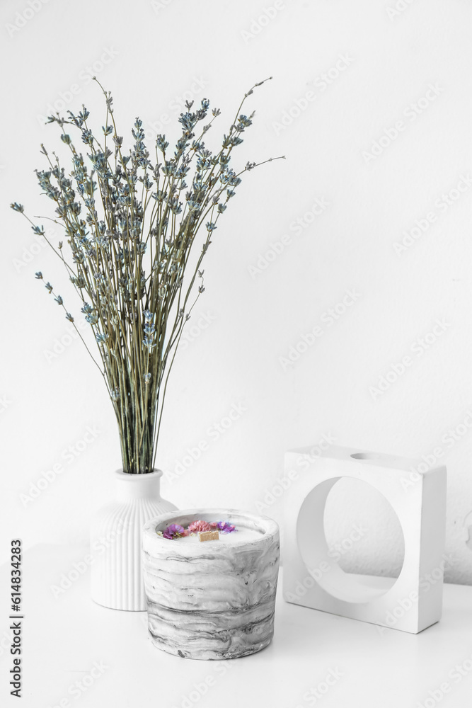 Lavender flowers and candle on table near light wall in room, closeup