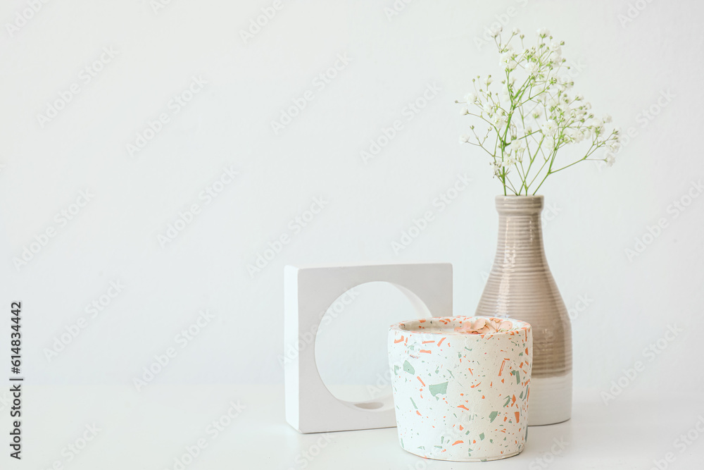 Gypsophila flowers and candle on table near light wall in room, closeup