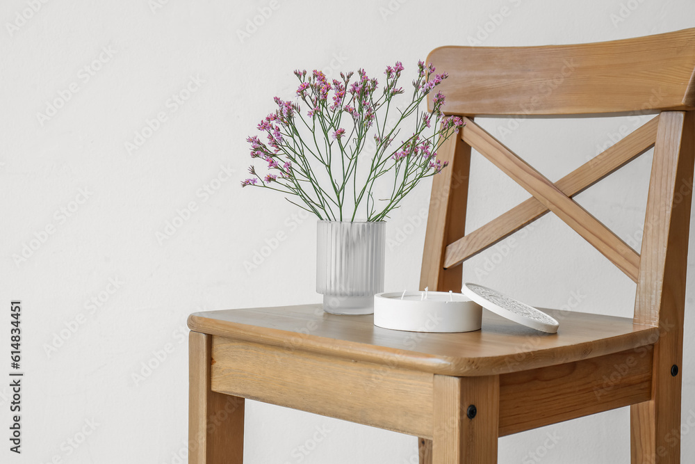 Beautiful flowers and candle on chair near light wall in room, closeup