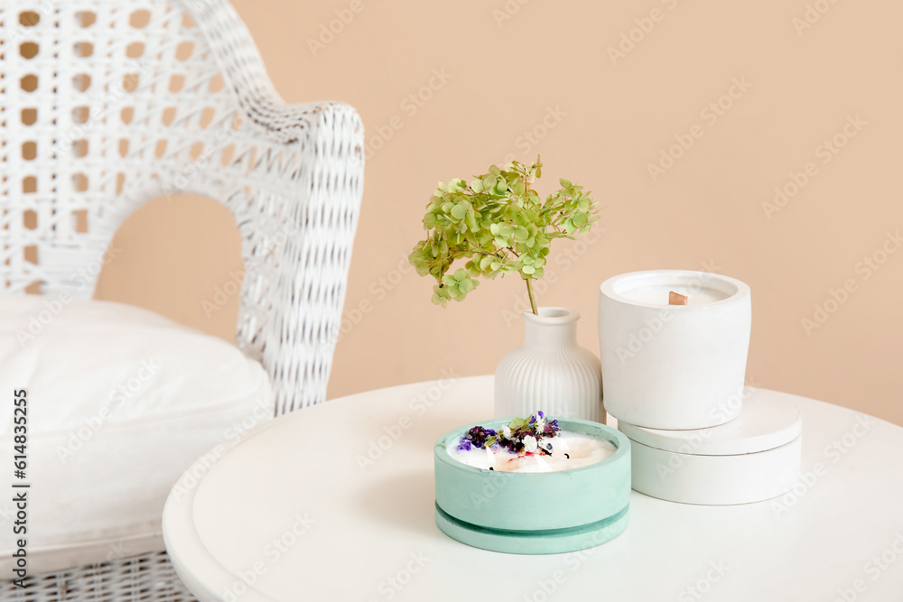 Hydrangea flowers, candles on table and chair near beige wall in room, closeup