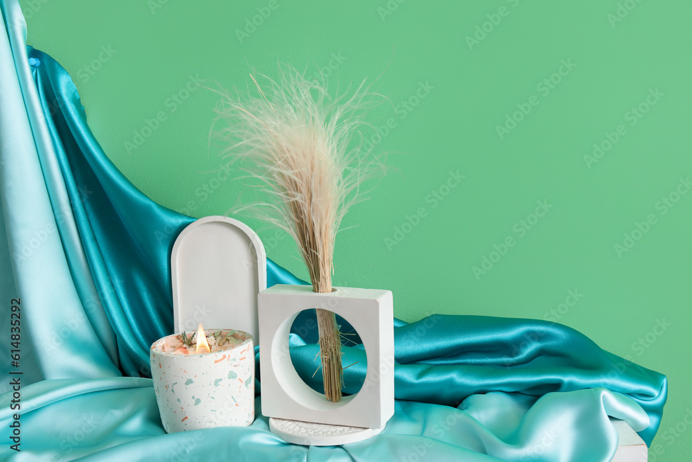 Pampas grass, blanket and burning candle on table near green wall in room