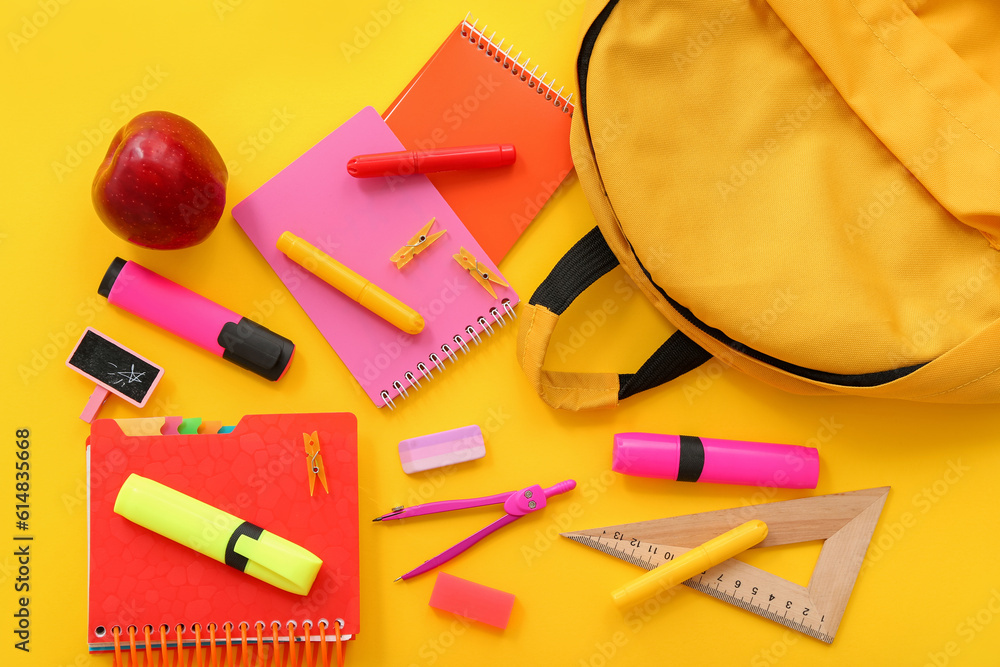 Backpack with fresh red apple and different stationery on yellow background