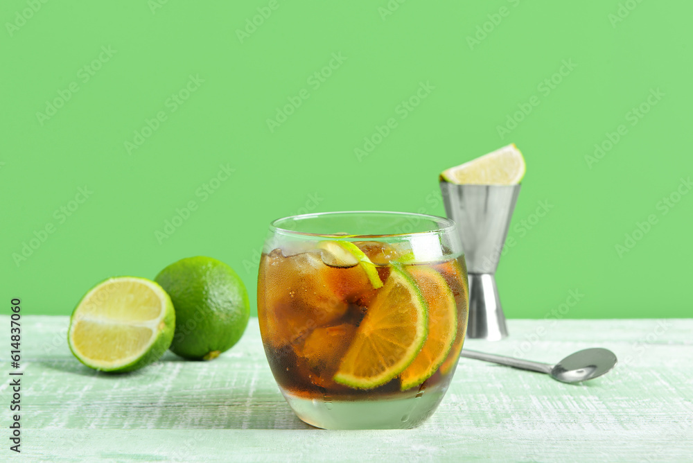 Glass of cold Cuba Libre cocktail and limes on green wooden table