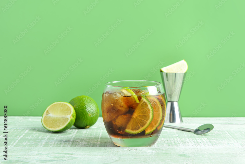 Glass of cold Cuba Libre cocktail and limes on green wooden table