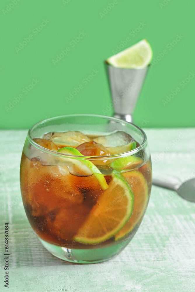 Glass of cold Cuba Libre cocktail on green wooden table