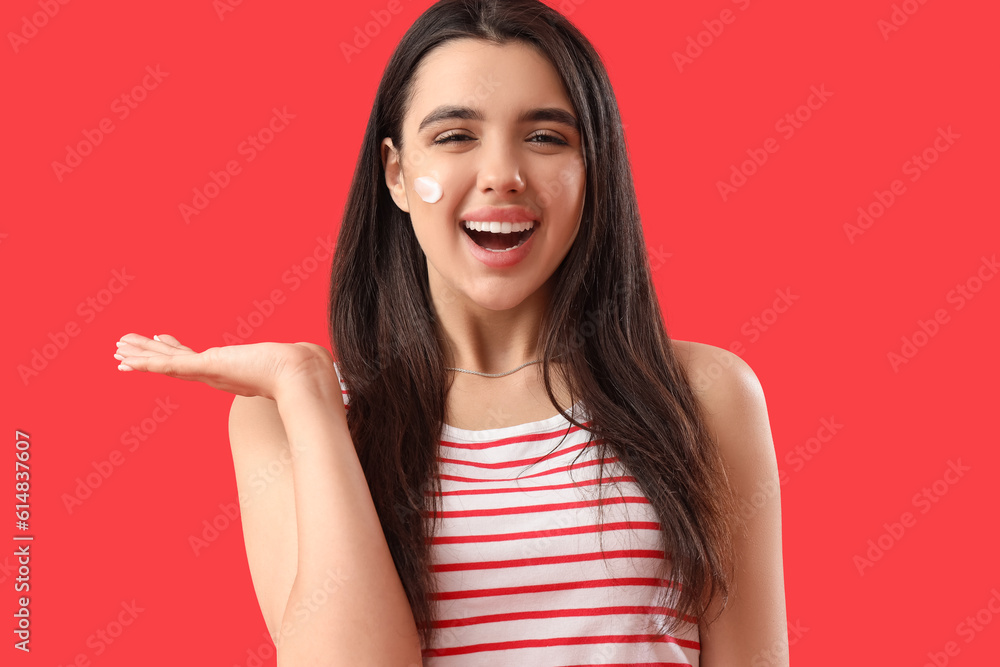 Young woman with sunscreen cream on her face against red background, closeup