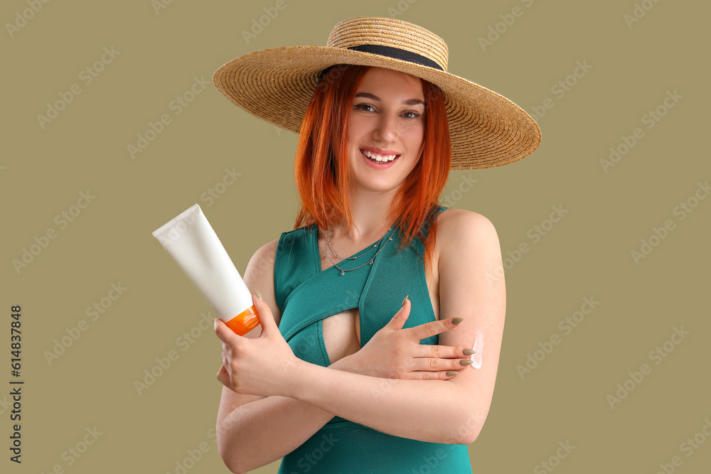 Young woman applying sunscreen cream on green background