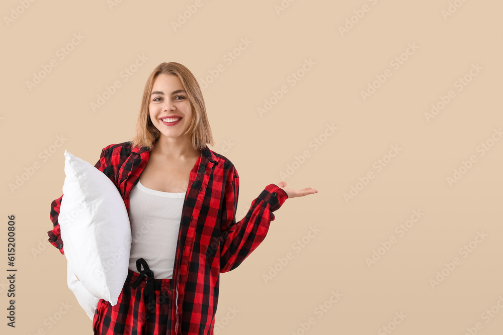 Young woman in pajamas with pillow showing something on beige background