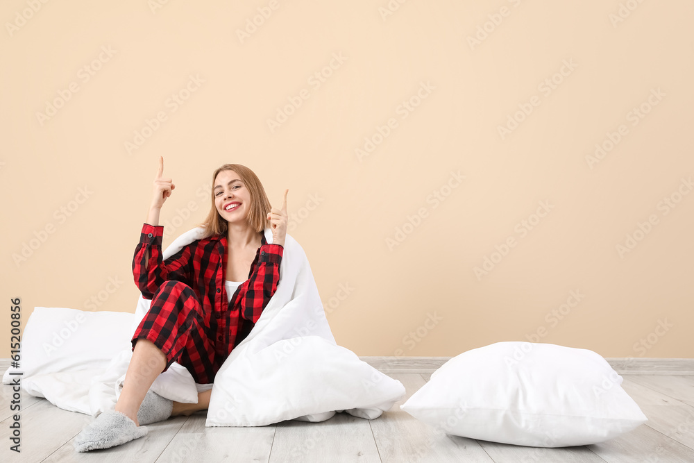 Young woman in pajamas with blanket pointing at something near beige wall