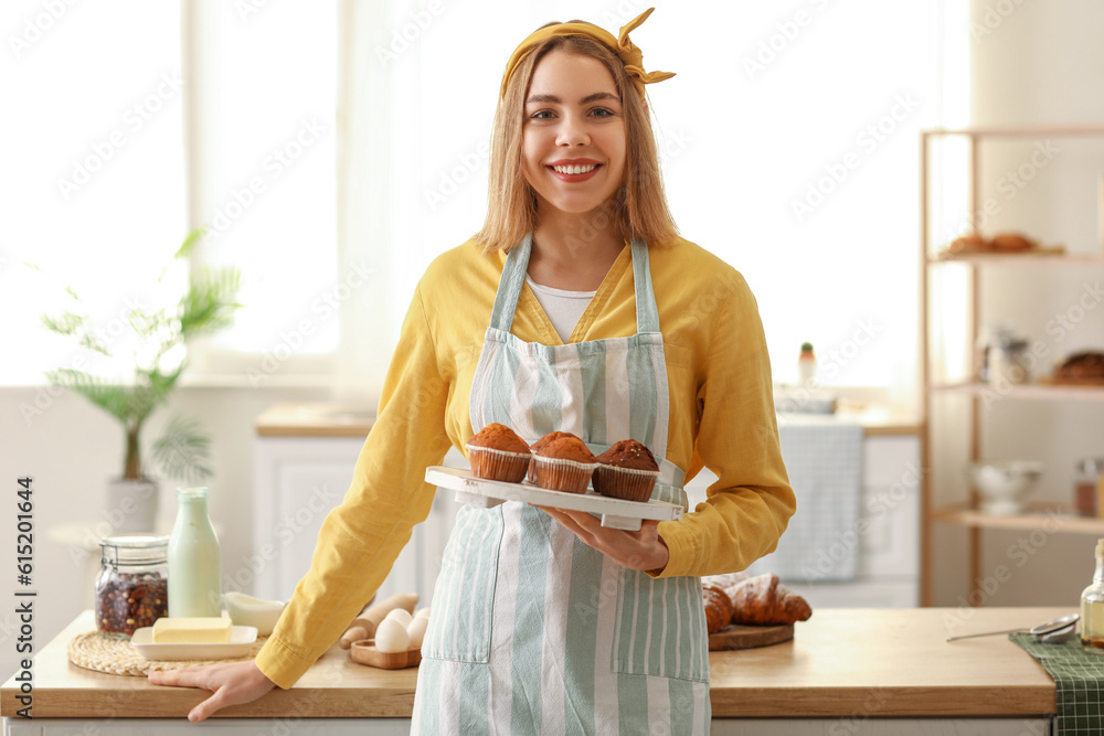 Female baker with tray of tasty cupcakes in kitchen