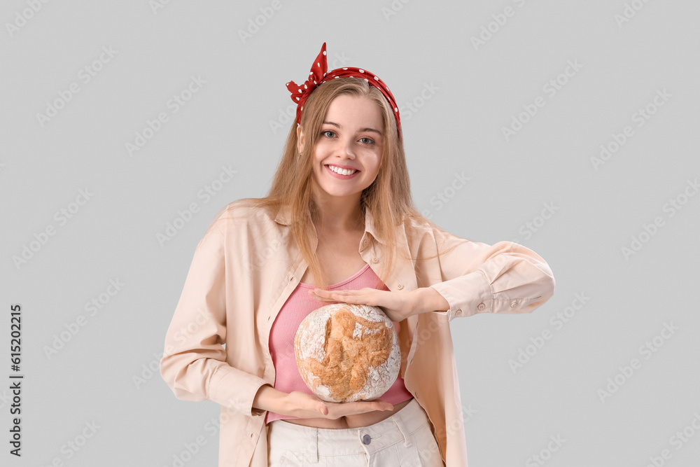 Young woman with fresh bread on grey background