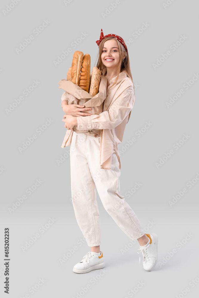 Young woman with fresh baguettes on grey background