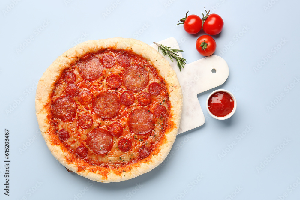 Board with delicious pepperoni pizza, tomatoes and sauce on blue background