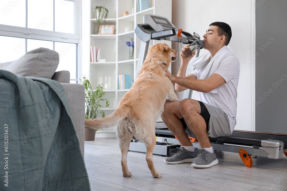 Sporty young man with cute Labrador dog drinking water at home