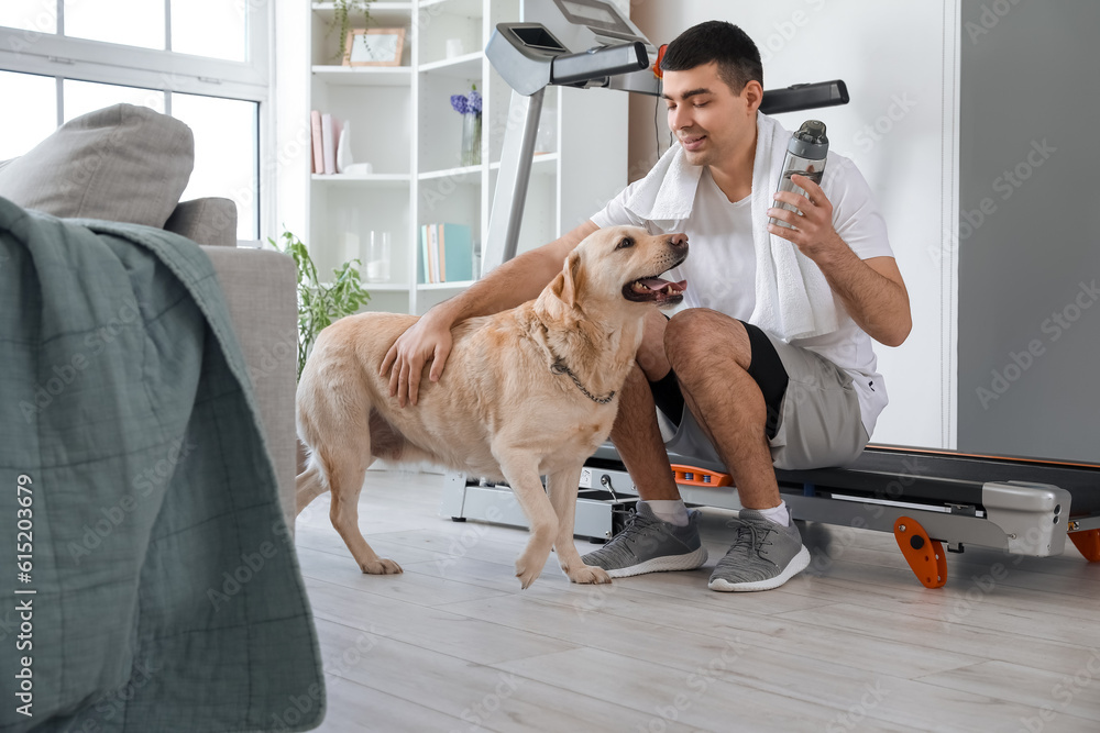 Sporty young man with bottle of water and cute Labrador dog at home