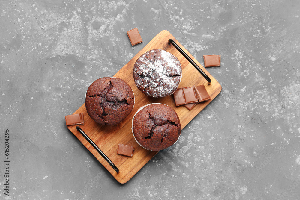 Wooden board with tasty chocolate cupcakes on blue background