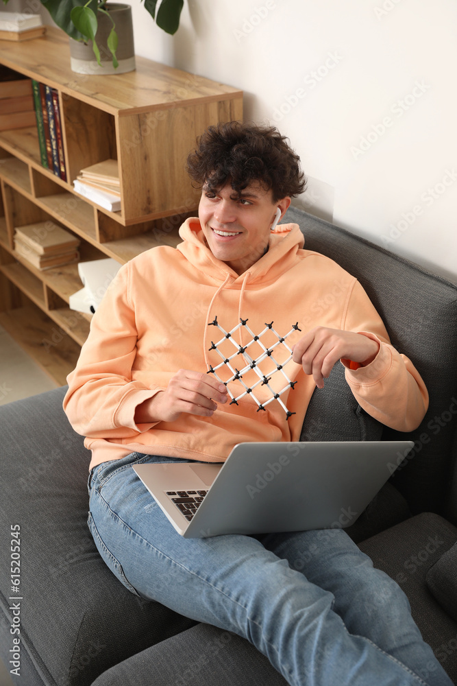 Male student with molecular model and laptop at home