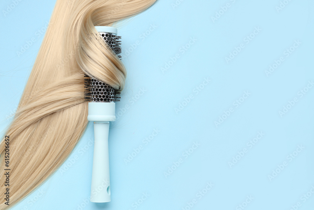 Round hair brush with blonde strand on blue background