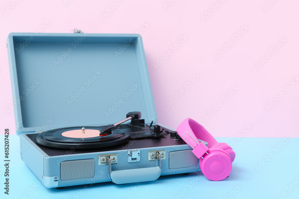 Record player with vinyl disk and headphones on table near pink wall