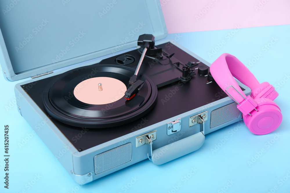 Record player with vinyl disk and headphones on table near pink wall