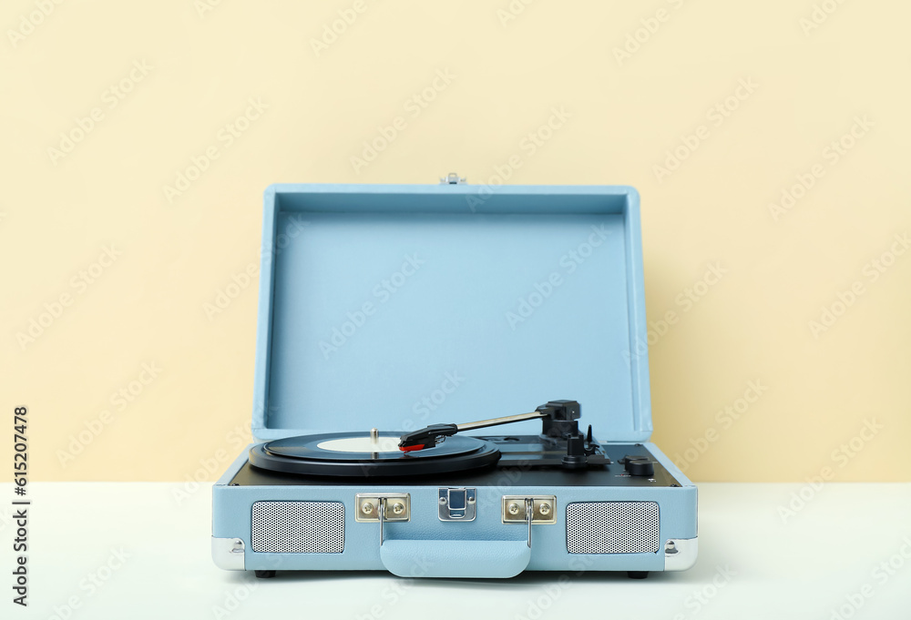 Record player with vinyl disk on table near beige wall